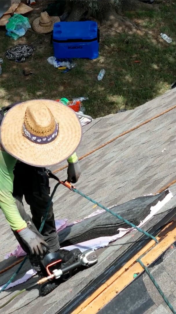 Overhead drone view of a roofer nailing off a shingle course.